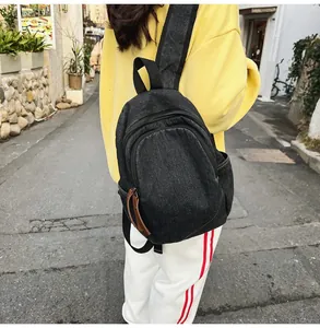 Rear view of a vintage washed denim backpack with leather zipper tabs in a street setting