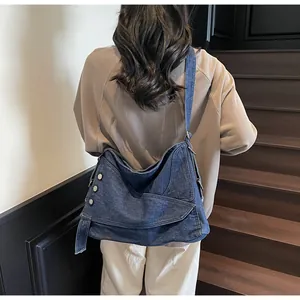 Detail of blue denim crossbody bag with metal rivets and asymmetrical layered design