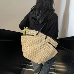 Beige woven straw tote bag with black trim on grey stairs, casual beach style
