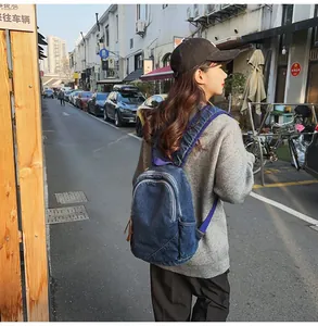 Outdoor street view of a dark blue denim backpack worn by a model from a side angle