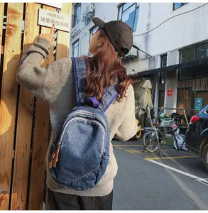 Detail of blue denim backpack showing double zippers and purple straps on a street background
