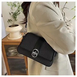 Close-up of black crossbody bag with woven texture and round silver buckle on beige blazer