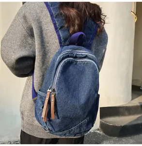 Detail of dark blue denim backpack featuring leather zipper pulls and purple edge trim