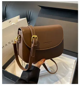 Close-up of brown leather shoulder bag with adjustable gold buckle and embossed text