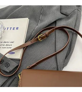 Detail of adjustable brown leather shoulder strap with golden metal buckle and stitching