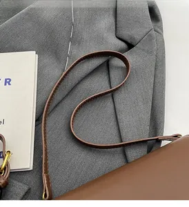 Detail of dark brown leather shoulder bag strap with golden metal buckle on gray blazer