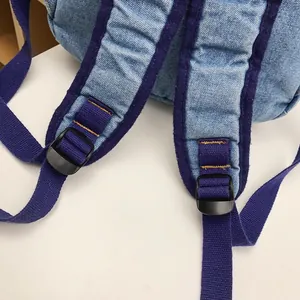 Blue denim backpack with adjustable purple canvas straps and reinforced yellow stitching