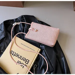 Close-up of pink woven crossbody bag with pearl knot detail on leather jacket background