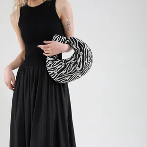 Detail of zebra pattern crescent bag with silver rivets held by a model in a black dress