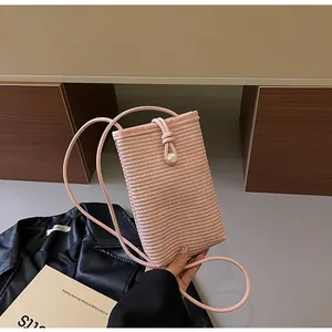 Detail of pink straw woven crossbody phone bag held by hand in a lifestyle setting