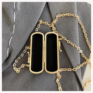Close-up of golden metal lipstick case with black velvet lining and chain strap