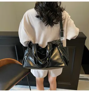 Detail of black glossy PU leather tote bag with pleated design and adjustable shoulder strap