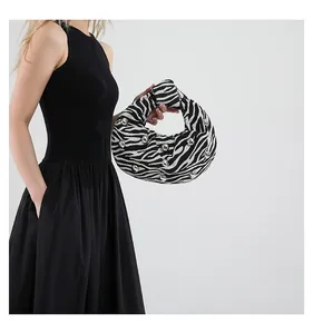 Detail of zebra print knot bag with silver studs held by a model in a black dress
