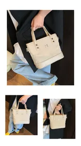 Close-up of beige canvas and leather tote bag featuring a metal M logo and stud detail