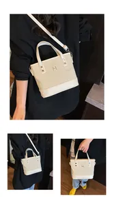Detail of cream canvas tote bag featuring metal letter logo and adjustable shoulder strap