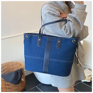 Détail d'un grand sac cabas en denim avec poignées en cuir porté à l'épaule par un mannequin