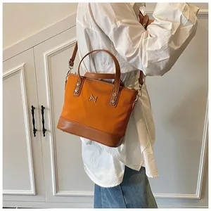 Detail of orange tote bag with leather straps and metal M logo on white background
