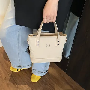 Minimalist beige canvas tote bag with M logo shown in a stylish handheld fashion scene