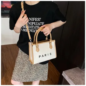 Detail of canvas tote bag with brown leather handles and black PARIS print