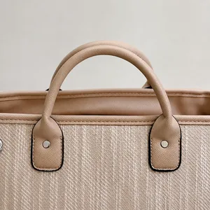 Macro detail of beige woven fabric bucket bag with brown Saffiano leather handle and rivets