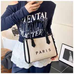 Detail of woven beige tote bag with black leather handles and Paris print on the side