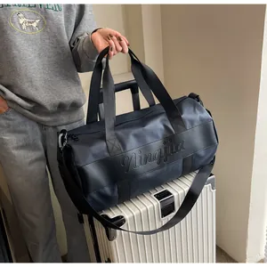 Dettaglio del logo in rilievo sulla grande borsa da viaggio scura sopra una valigia
