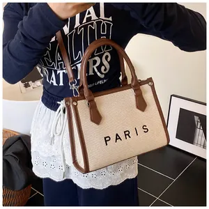 Detail of woven tote bag featuring Paris logo, brown leather trim, and adjustable strap