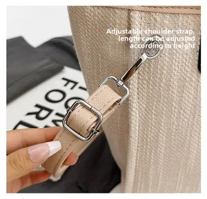 Detail of adjustable beige faux leather strap with metallic buckle on woven bucket bag