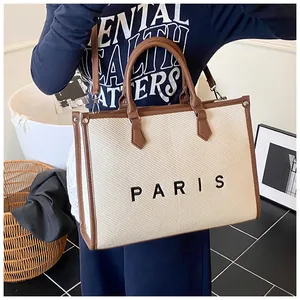 Detail of minimalist cream woven tote bag with brown leather trim and PARIS lettering