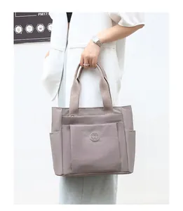 Detail of grey-purple nylon tote bag showing front zip pocket and side utility compartments
