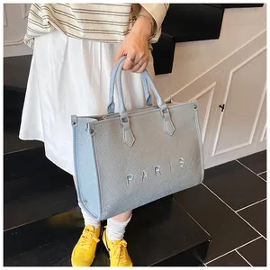 Detail of grey-blue woven tote bag with Paris embroidery and leather handles