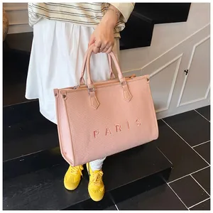 Close-up of pink woven tote bag featuring embroidered Paris text and leather handles