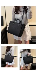 Detalle de bolso tote negro con textura trenzada, asas dobles y correa de hombro