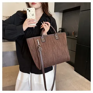 Detalle del bolso tote marrón tejido con asas de cuero oscuro y correa de hombro ajustable