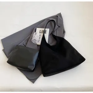 Flat lay of black suede tote bag set with a laptop, grey suit, and minimal life book