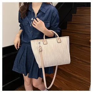 Detalle del bolso tote tejido con asas de cuero marrón llevado por modelo en vestido denim