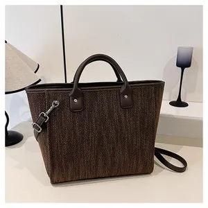 Detalle del bolso tote tejido marrón oscuro con asas de cuero y herrajes plateados