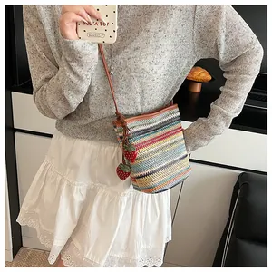 Détail du sac seau tissé à rayures colorées avec pendentifs fraises et bandoulière en cuir