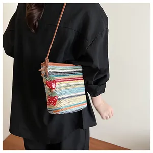 Détail du sac seau en paille à rayures colorées avec breloques fraises et bandoulière