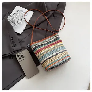 Détail d'un sac seau en paille à rayures colorées avec des anses en similicuir marron