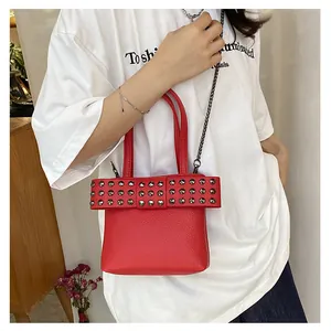 Détail d'un sac rouge en cuir à motifs lychee avec clous métalliques porté par un mannequin