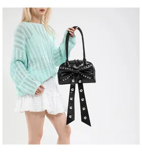 Close-up of black leather shoulder bag featuring a large bow and silver stud details