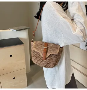 Detail van geweven strooien crossbodytas met bruine leren riem en gouden metalen gesp