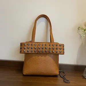 Sac à main marron en cuir grainé avec grand nœud clouté et bandoulière en chaîne sous lumière