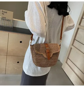 Detail van geweven strooien crossbody tas met bruine leren riem en metalen gesp