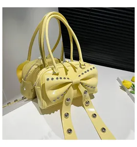 Detail shot of yellow shoulder bag with large bow and silver rivet studs on white surface