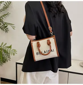Modellansicht der beigen Canvas-Tasche mit braunem Lederbesatz und BULAIDAI-Logodruck
