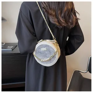 Détail du sac rond en dentelle blanche avec perles et bandoulière dorée sur tenue noire