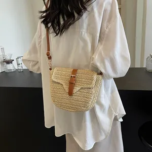 Gevlochten strooien zadeltas met bruine leren riem gedragen door een model in een kamer