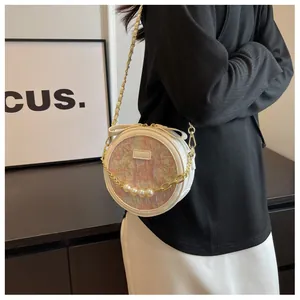 Détail d'un sac à bandoulière rond beige avec chaîne en perles et tissu à motif peinture